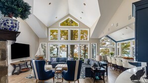 Un salón espacioso con techo alto, ventanas grandes y vistas a árboles.