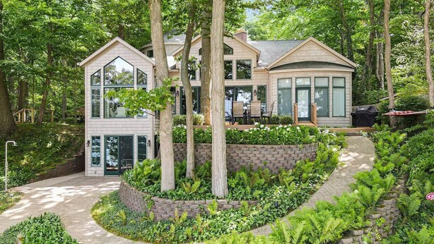 Una casa moderna con un camino de entrada curvo, rodeada de exuberante vegetación y árboles.