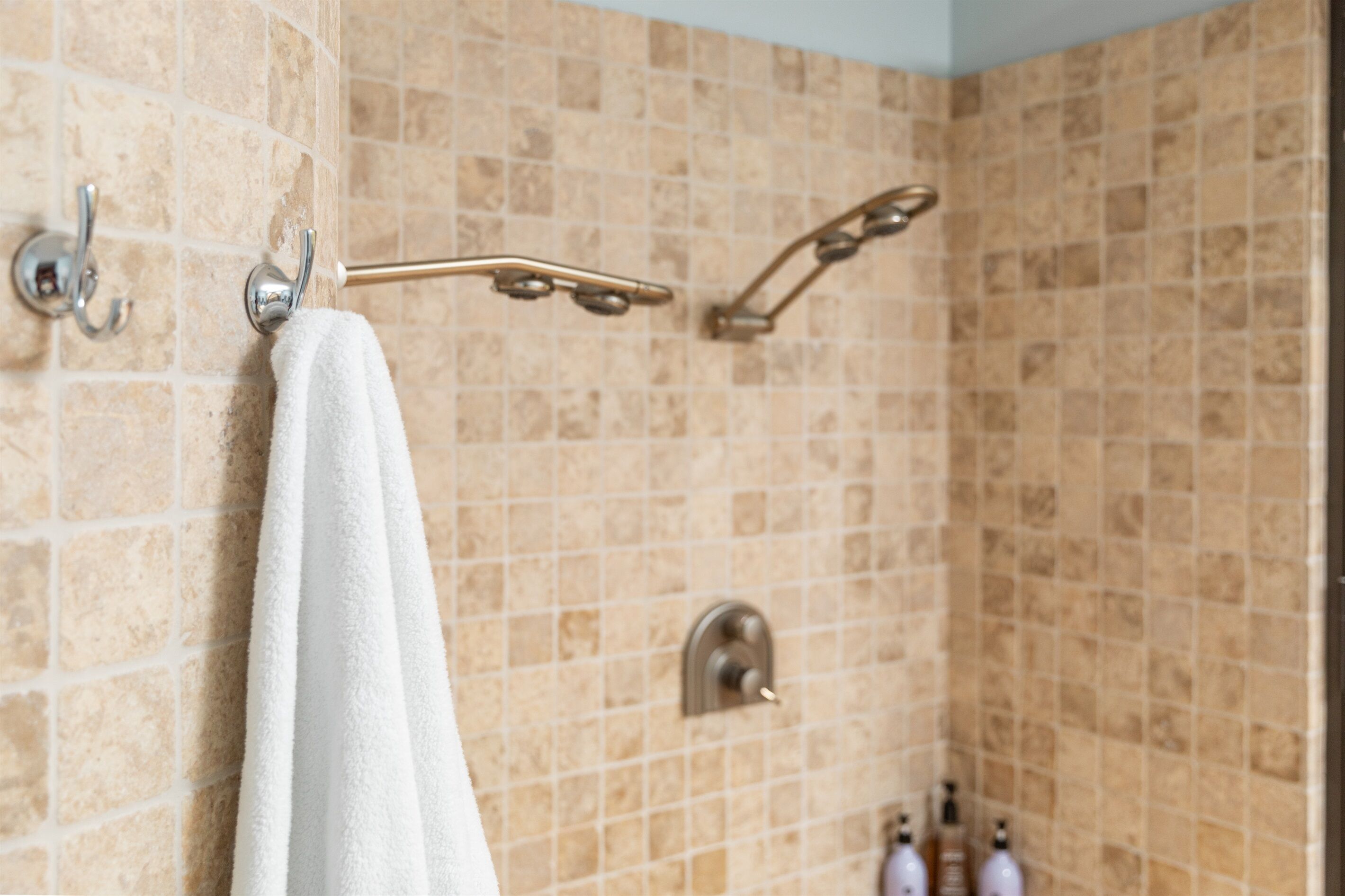 A bathroom with beige tiled walls, a white towel hanging on a rack, and a showerhead.