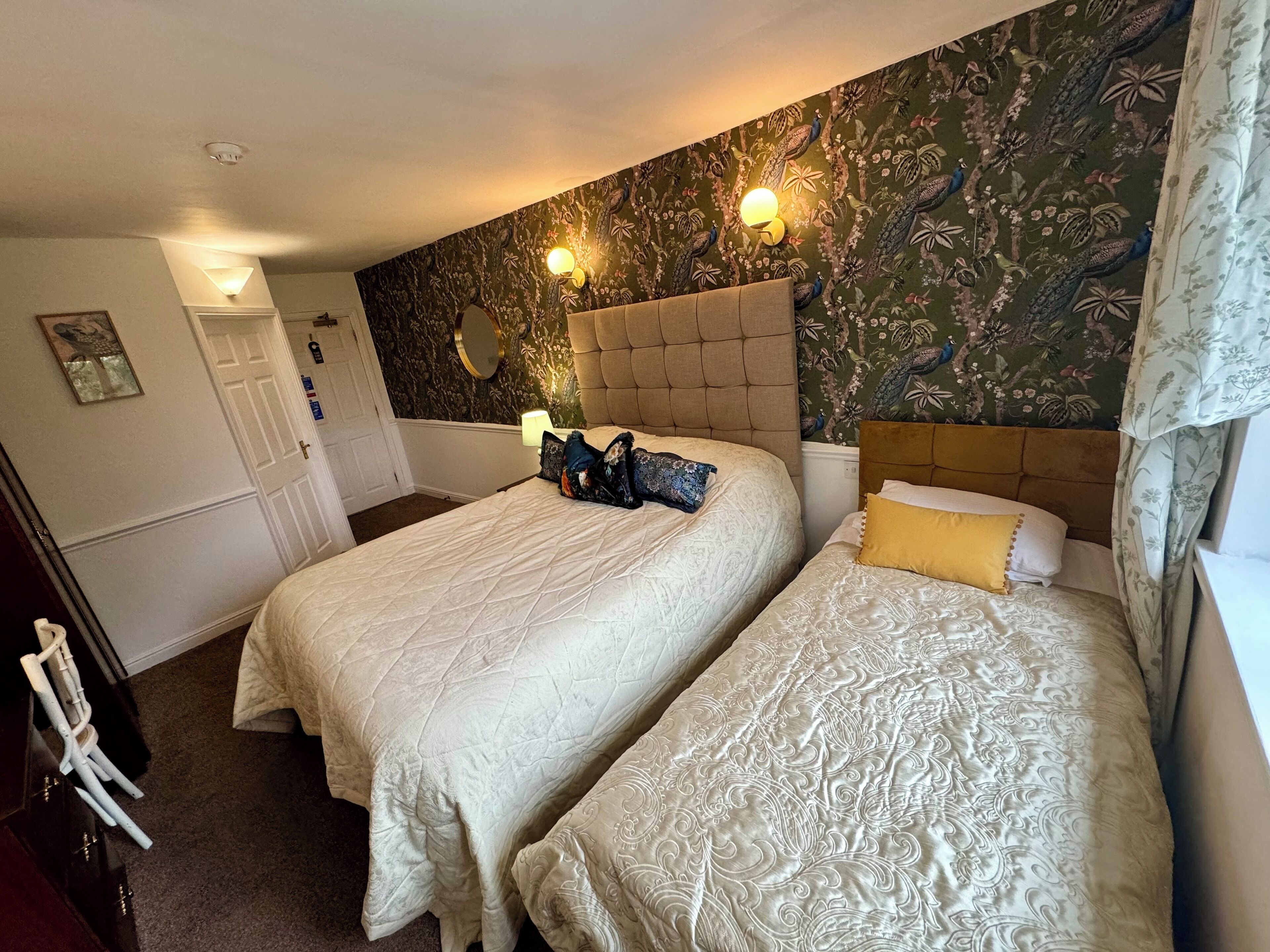 A room with two beds, a mirror, and a wall with a peacock pattern.