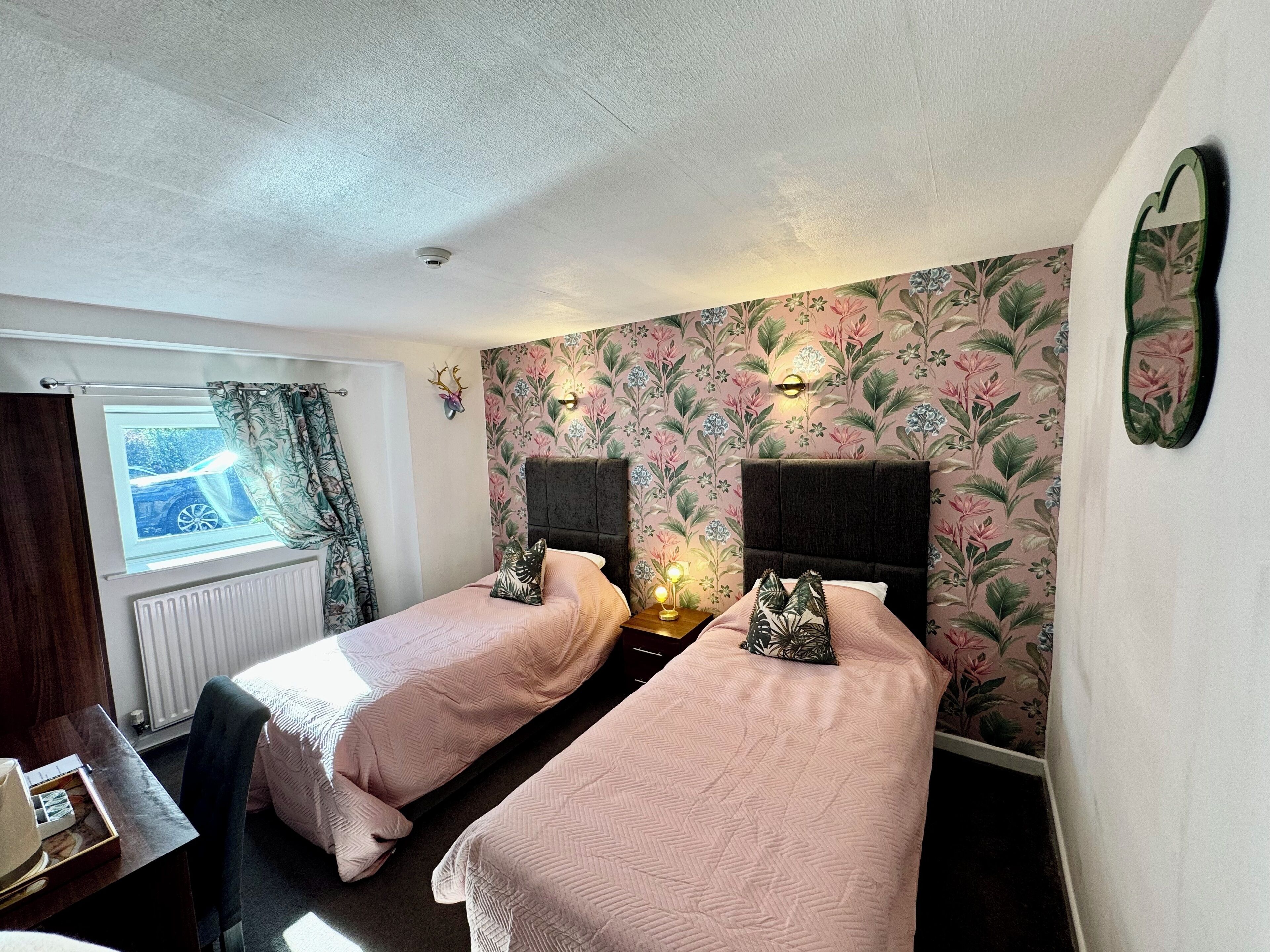 A room with two single beds, a window with curtains, a radiator, and a wall-mounted light fixture.