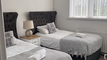 Un dormitorio con dos camas, una mesita de noche, una lámpara y un ventanal con persianas.