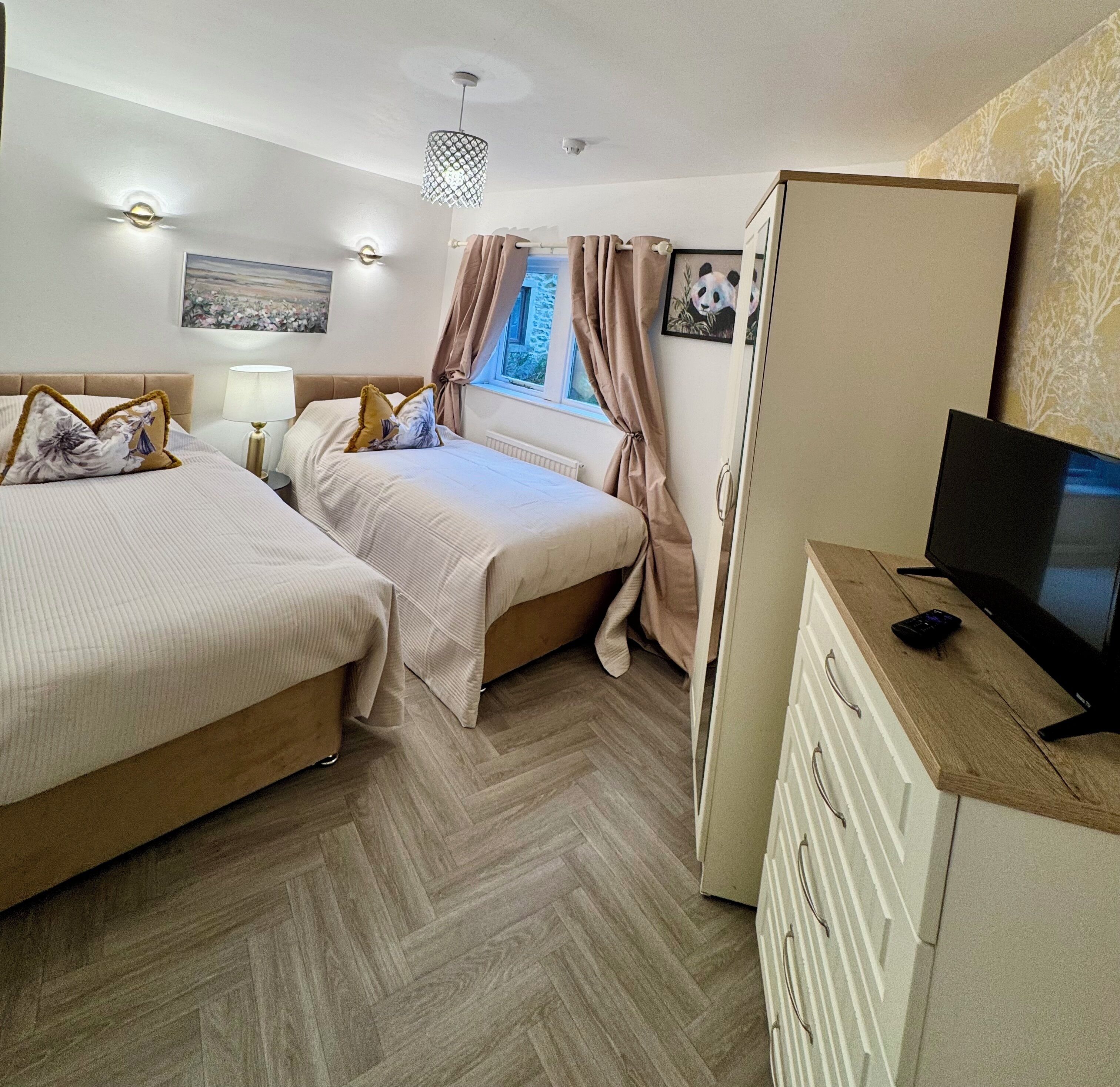 A hotel room with two beds, a TV, a dresser, and a window with curtains.