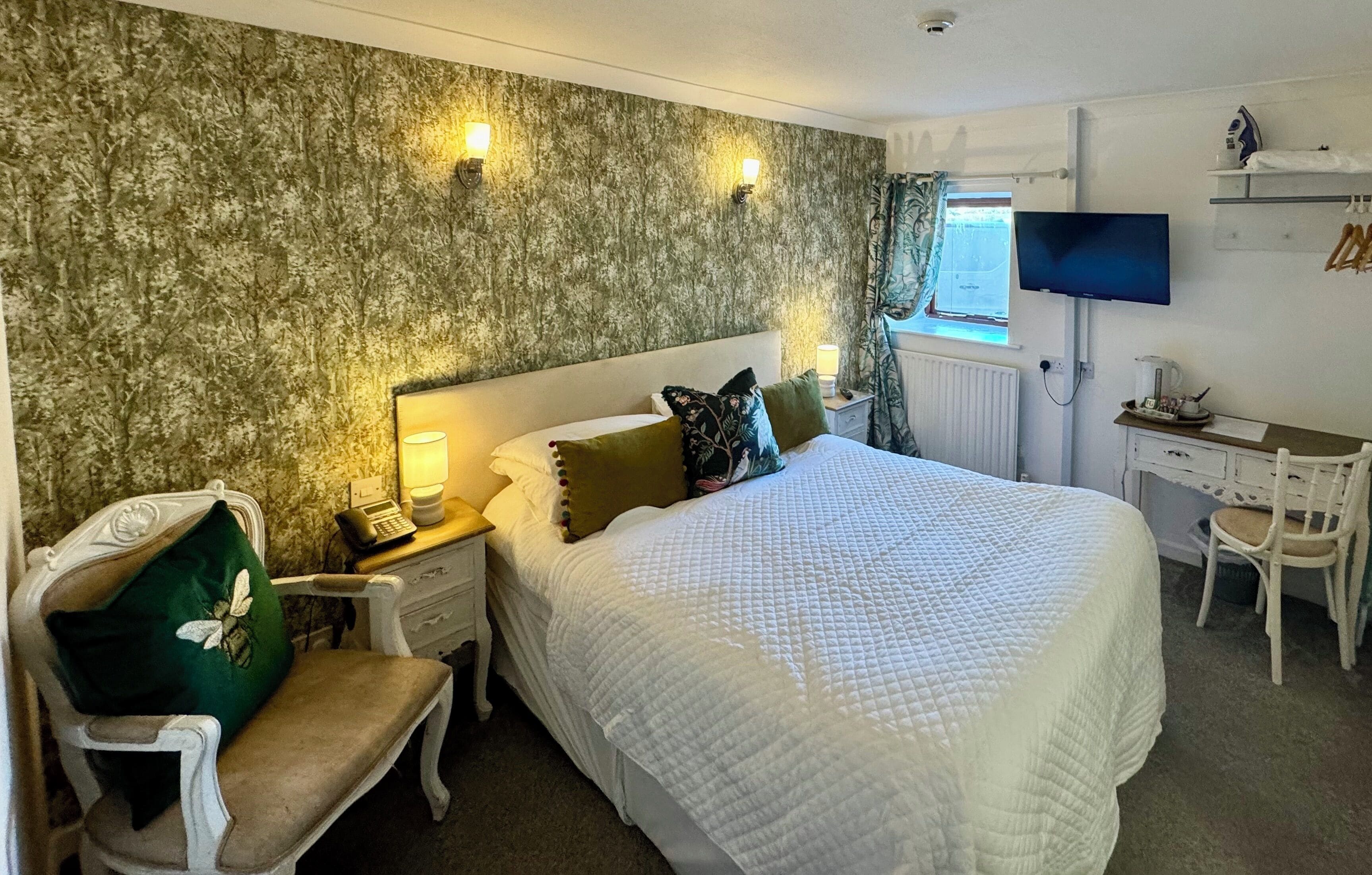 A hotel room with a large bed, a desk with a computer, a chair, a lamp, and a television.