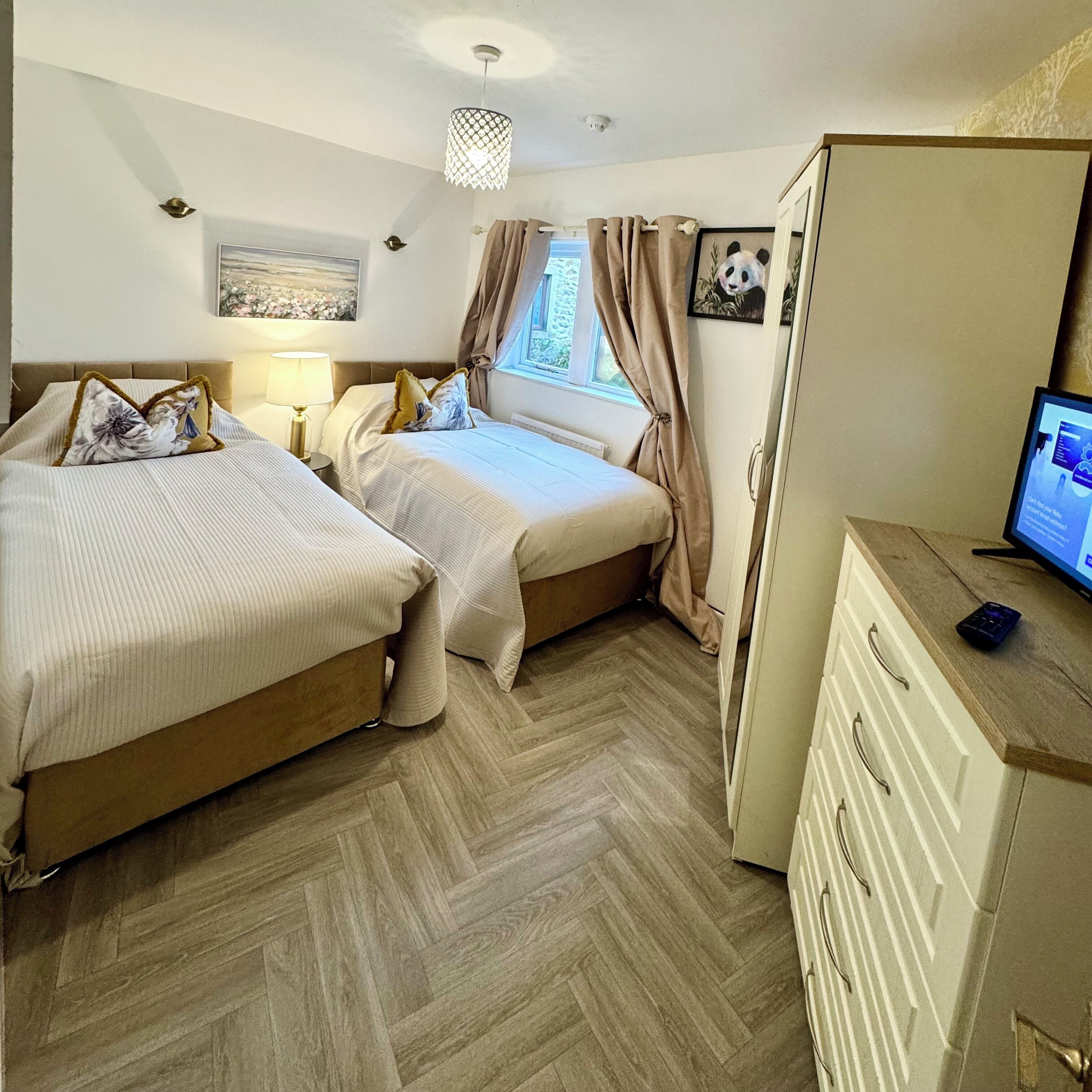 Habitación de hotel con dos camas, un escritorio con ordenador, un armario y una ventana con cortinas.