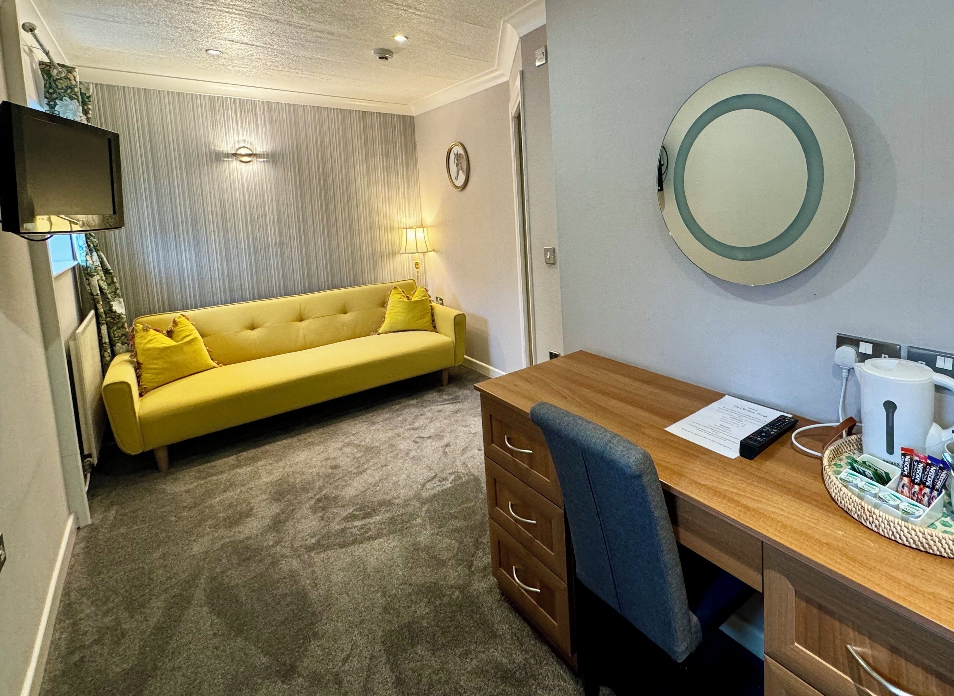 A room with a yellow sofa, a wooden desk, a mirror, and a lamp.