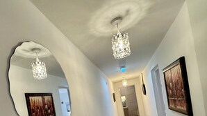 Un pasillo con piso de madera en diseño de espiga, un espejo ovalado grande y dos candelabros.