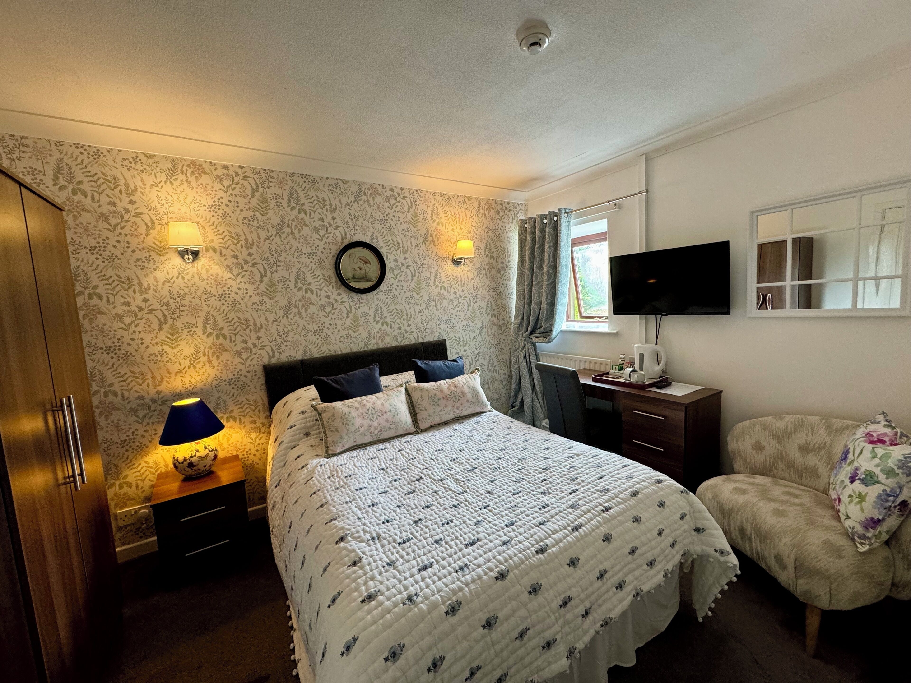 Un dormitorio con cama, lámparas de noche, escritorio con silla, televisor y ventana con cortinas.