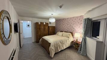 Een slaapkamer met een bed, een kledingkast, een spiegel, een kroonluchter, een raam met gordijnen en een deur naar een andere kamer.