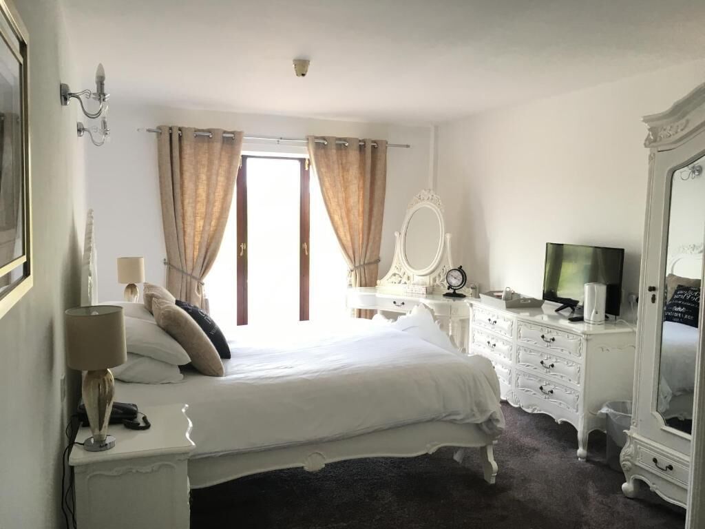 A bedroom with a bed, a dresser, a mirror, a television, and a window with curtains.