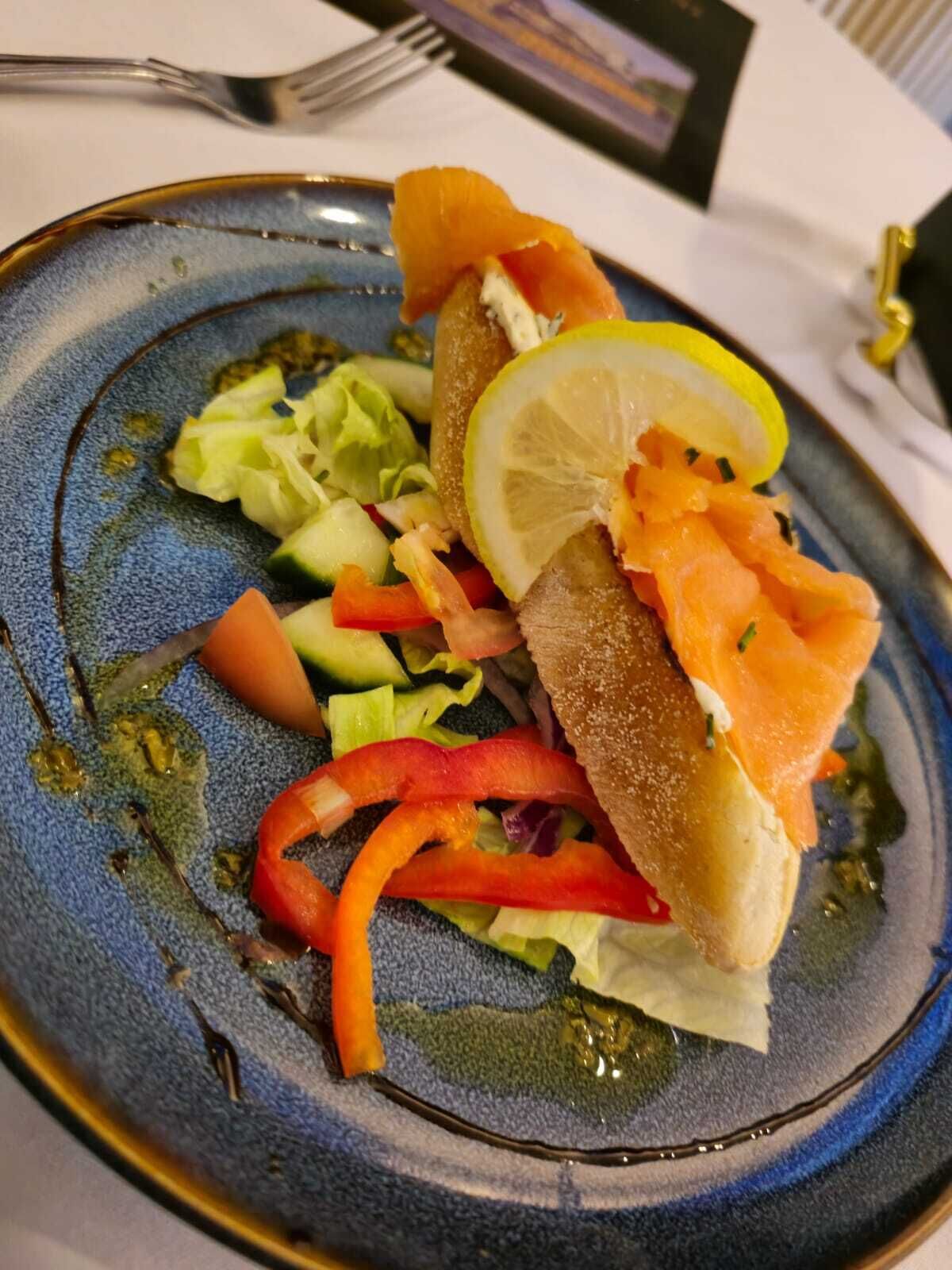 Une assiette de saumon fumé, accompagnée de pain, de citron et de légumes.