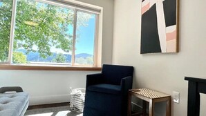 A room with a large window, a blue chair, a small wooden table, and a painting on the wall. - Summit Lofts, 2 Queen Beds, Mt Shasta #201 (Mt Shasta)