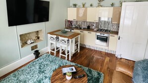 A compact living space with a dining area, kitchenette, and a TV mounted on the wall. - Charming 2-bedroom Apartment Located in Ayr (Ayr)