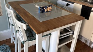 A kitchen with a wooden table, white chairs, a washing machine, and a dish rack. - Charming 2-bedroom Apartment Located in Ayr (Ayr)