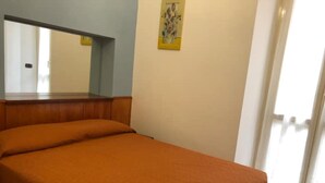 A room with a bed, a mirror, a painting, and a door.