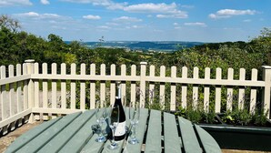 Une table avec une bouteille de vin et des verres, placée devant une clôture blanche en bois, avec en arrière-plan un paysage.