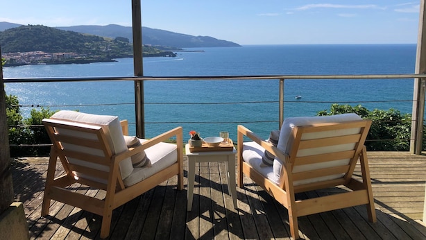Une terrasse en bois avec deux chaises longues donnant sur un paysage marin magnifique.