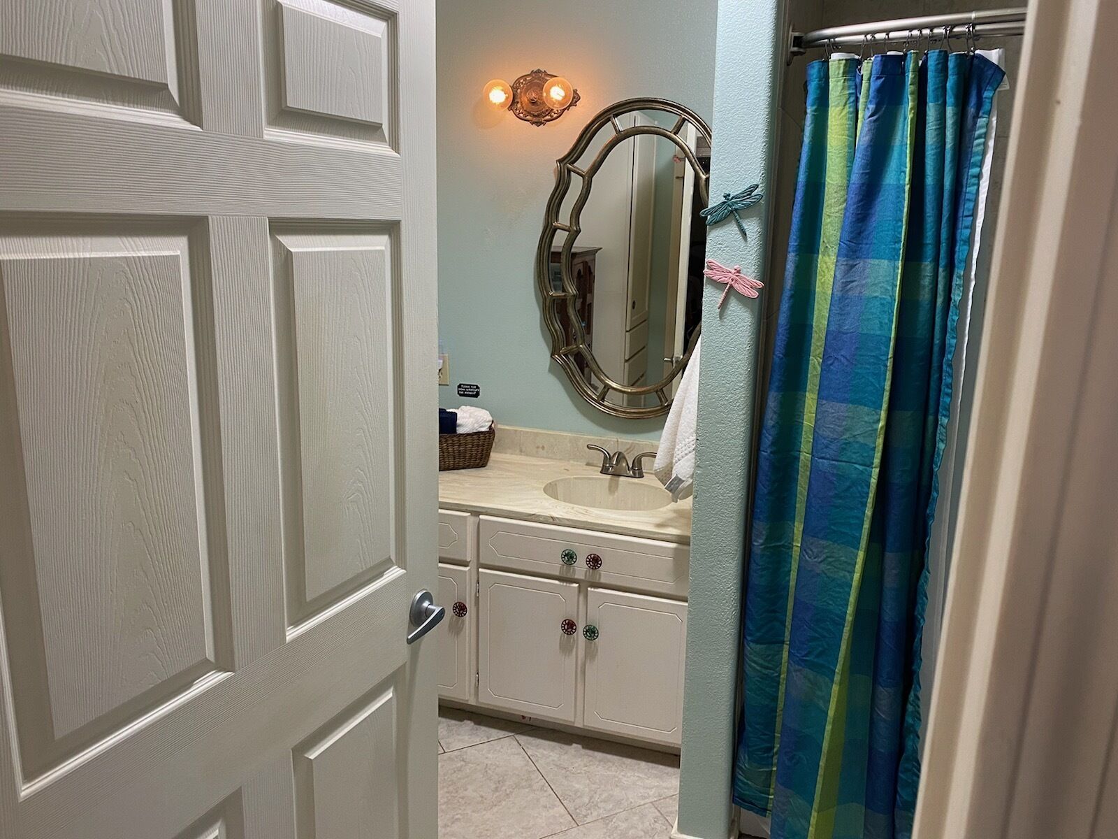 Une salle de bain avec une porte blanche, un lavabo, un miroir et un rideau de douche.