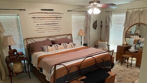 Een slaapkamer met een bed, nachtkastje, lamp, spiegel en een raam met jaloezieën.