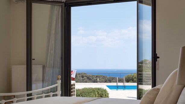 A bedroom with a large bed, a view of the sea, and a balcony with a pool.