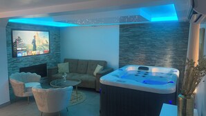 A modern living room with a flat-screen TV, a sofa, a glass coffee table, and a hot tub. - Sandspa 84 (Orange)