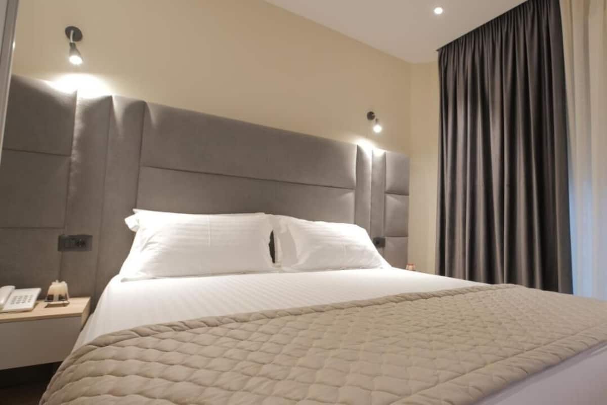 Une chambre d’hôtel avec un grand lit, une table de chevet avec un téléphone et une fenêtre avec des rideaux.