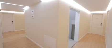 A modern, well-lit room with wooden flooring, white walls, and a door leading to another room.
