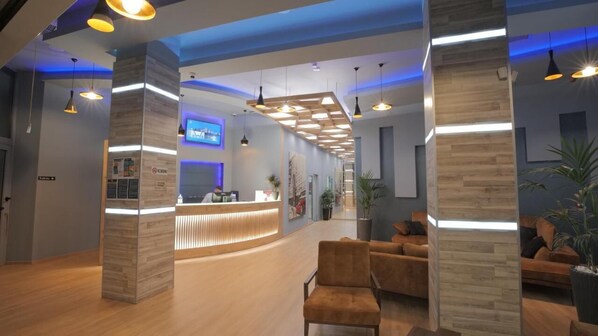 A modern reception area with a wooden reception desk, comfortable seating, and pendant lighting. - Granda Hotel (Kashar)