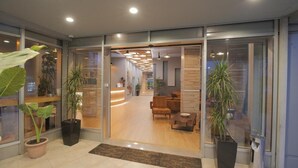 A modern reception area with glass doors, potted plants, and a seating area with sofas and a coffee table. - Granda Hotel (Kashar)