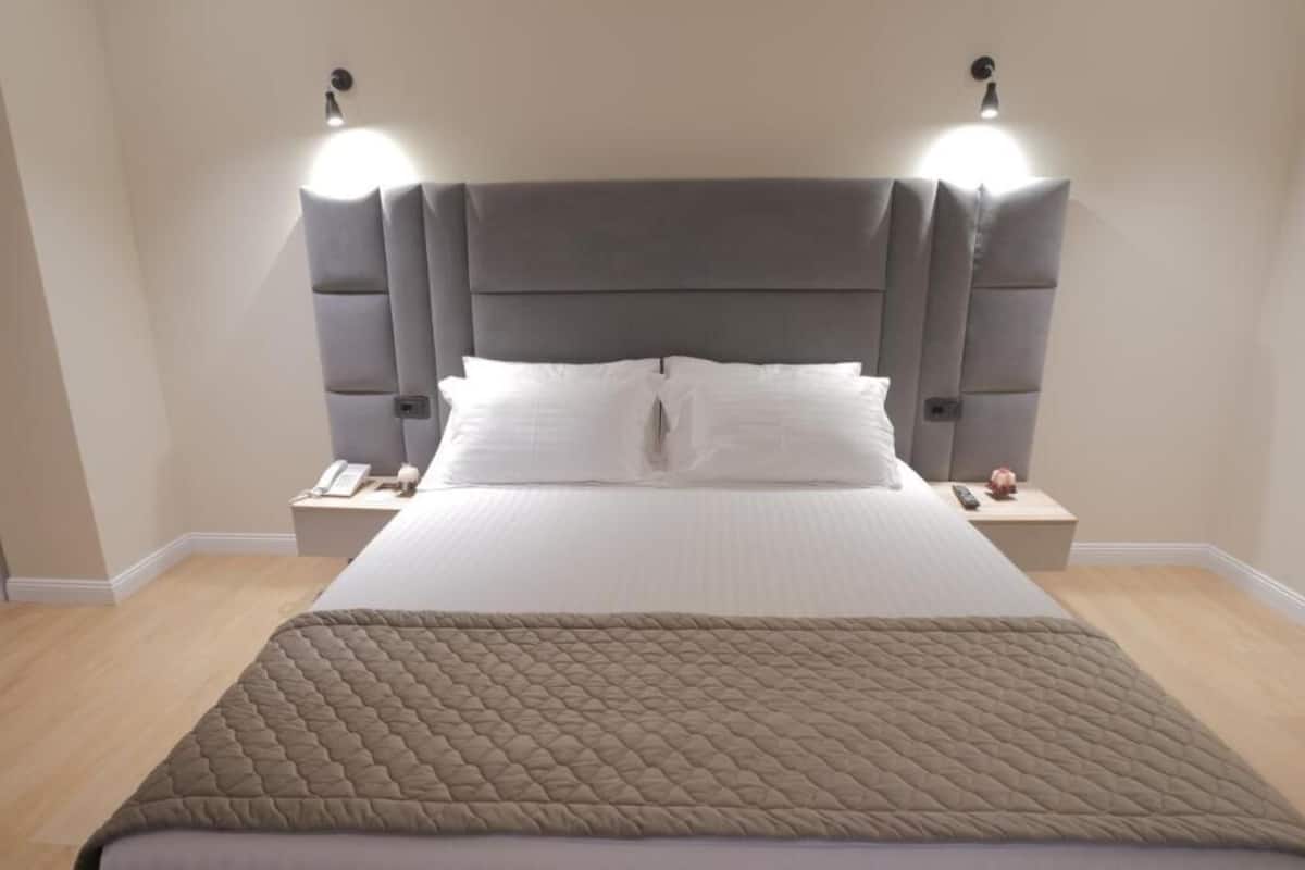Un lit bien fait, recouvert d’une courtepointe matelassée, avec deux tables de chevet dotées de lampes et une tête de lit pourvue d’un éclairage intégré.