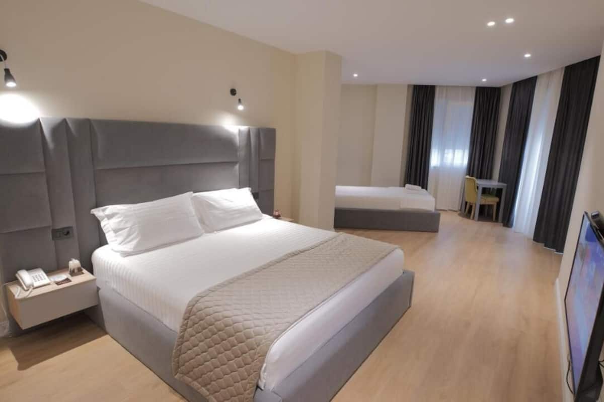 Une chambre d’hôtel moderne dotée d’un grand lit, d’une table de chevet avec un téléphone, d’un téléviseur à écran plat et d’un coin salon séparé avec une chaise et une table.