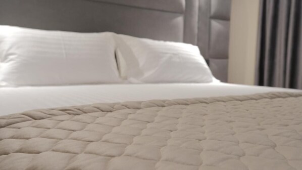 Una cama con cabecera acolchada y ropa de cama blanca.