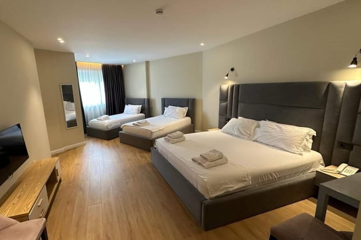 Une chambre d’hôtel avec deux lits simples, un grand lit, une télévision, un bureau et une chaise.
