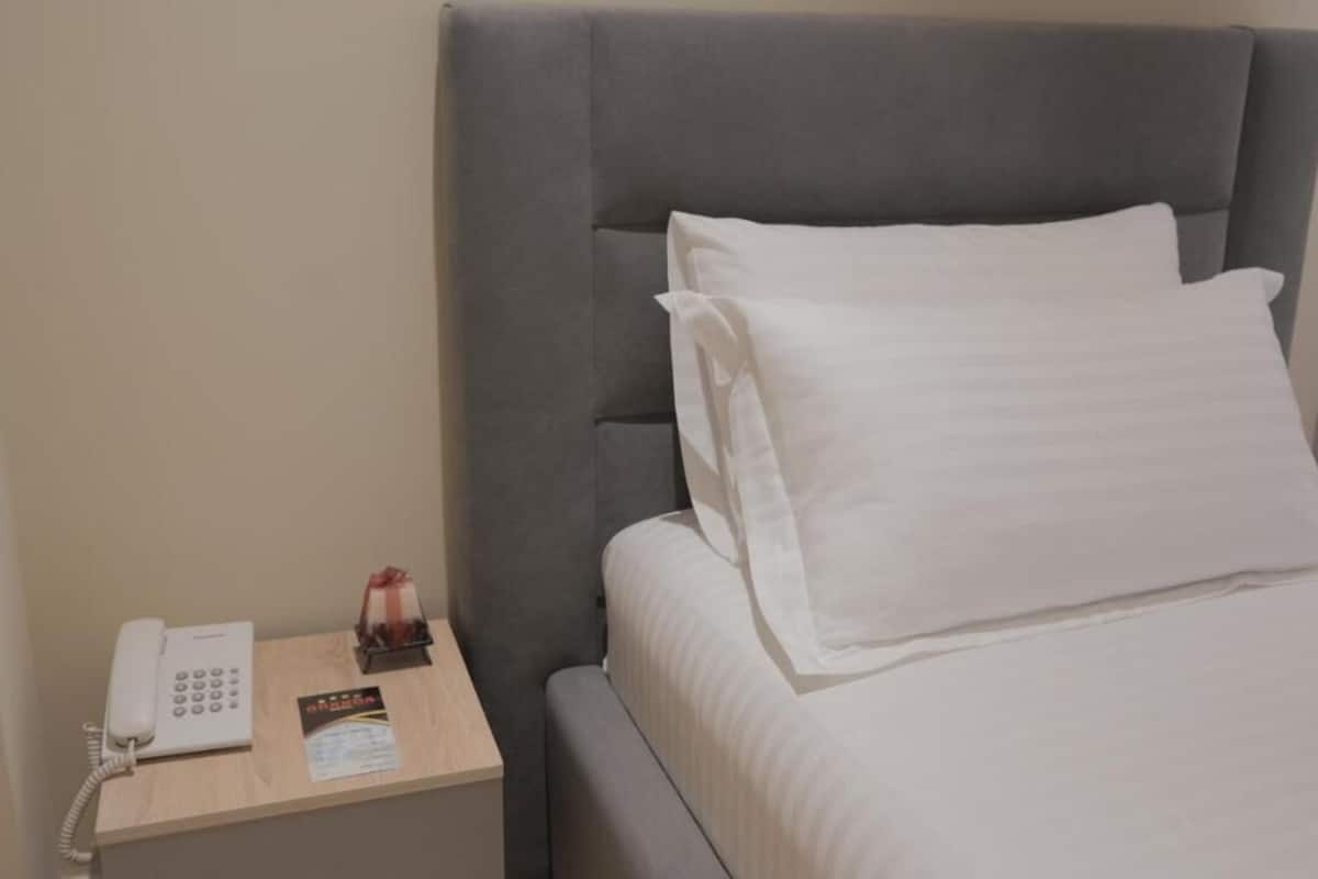 Une chambre d’hôtel avec un lit, une table de chevet avec un téléphone, une petite carte et un objet décoratif.