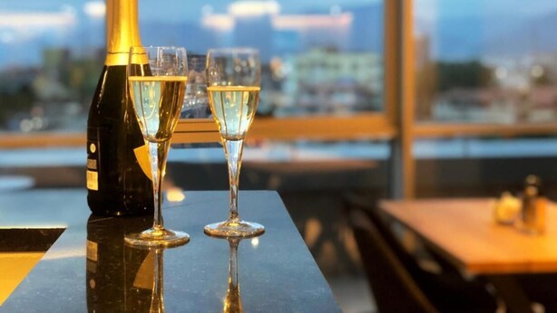 A bottle of champagne and two glasses on a table with a city view in the background. - Granda Hotel (Kashar)