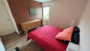 A bedroom with a bed, a wooden dresser, a painting on the wall, and a window.