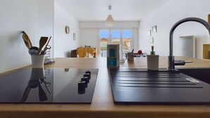 A modern kitchen with a black countertop, a sink, and a dining area in the background. - 200m from the beach, flat for 4 (Saint-Hilaire-de-Riez)
