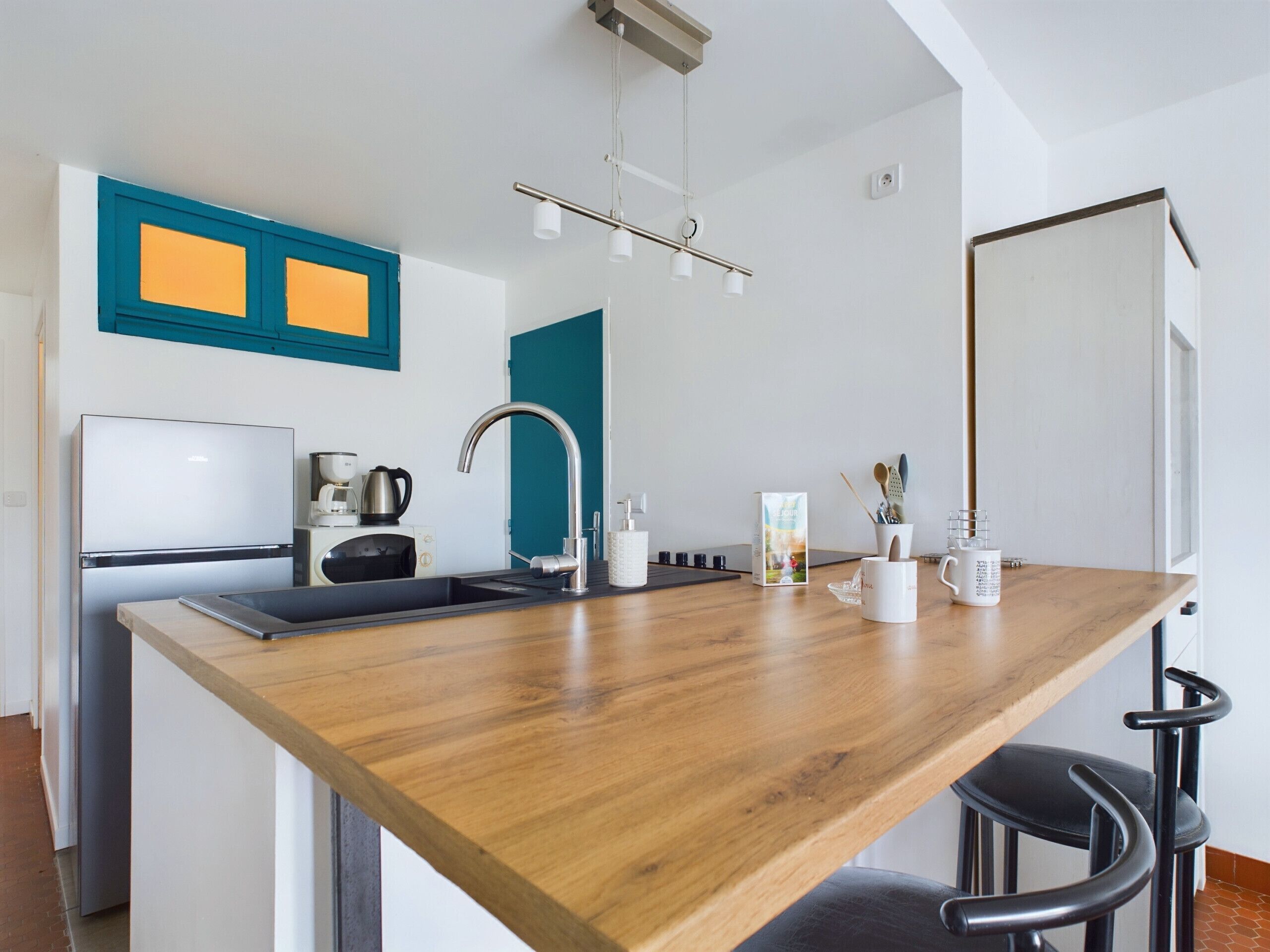 Une cuisine moderne avec un plan de travail en bois, des appareils électroménagers en acier inoxydable et un mur d’accent de couleur turquoise.