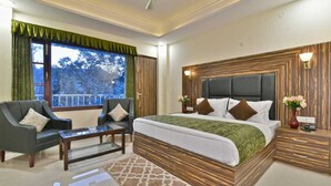 A bedroom with a large bed, two sofas, a coffee table, and a view of trees through the window. - Hotel Comfort Court (Dalhousie)