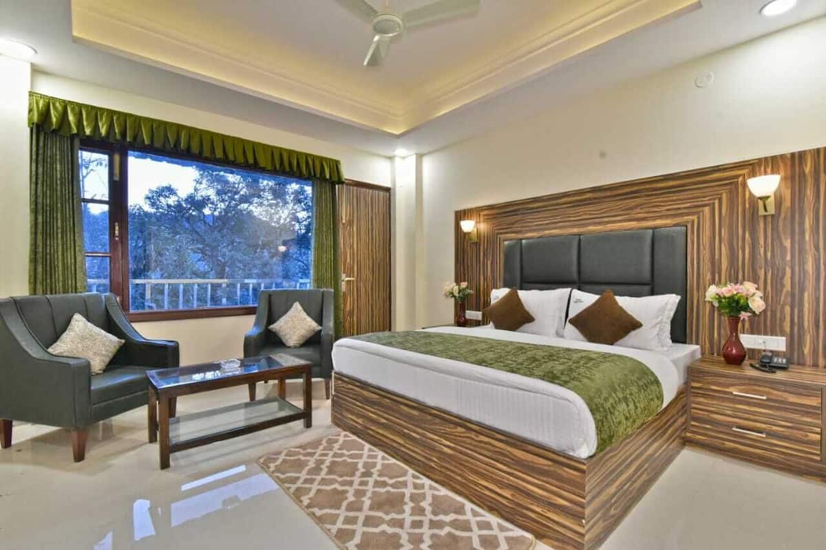 A bedroom with a large bed, two sofas, a coffee table, and a view of trees through the window.