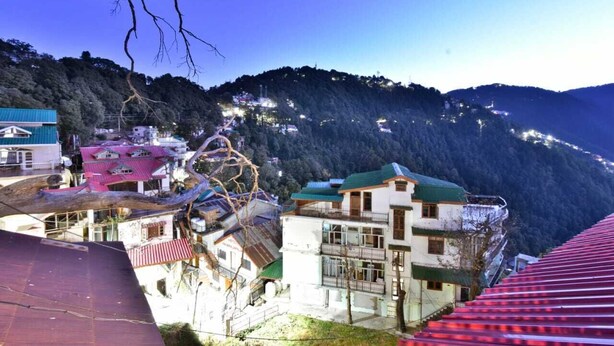 A mountainous area with buildings, including a multi-story structure with balconies and a building with a green roof. - Hotel Comfort Court (Dalhousie)