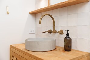 A bathroom with a round sink, a wooden countertop, a brass faucet, and a soap dispenser. - The Endless Summer Home - Where Waves and Town Unite (Mount Maunganui)