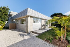 A modern single-story house with a flat roof, large windows, and a covered porch area. - The Endless Summer Home - Where Waves and Town Unite (Mount Maunganui)