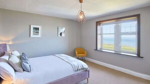 Une chambre dotée d’un grand lit, d’une fenêtre donnant sur la mer et d’un luminaire suspendu moderne.