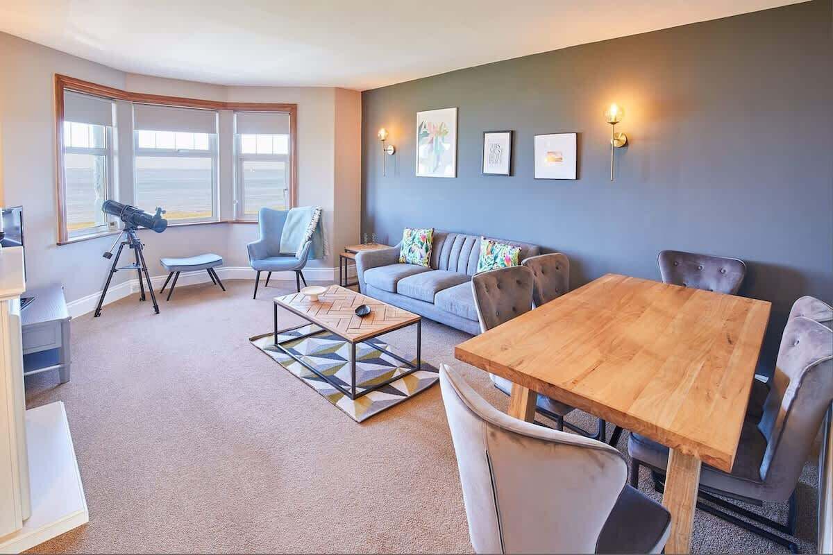 A modern living room with a large window, a telescope, a sofa, a coffee table, and a dining table.