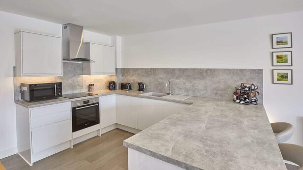 Une cuisine moderne avec des meubles blancs, un four encastré, un four à micro-ondes et un grand îlot central doté d’un évier.