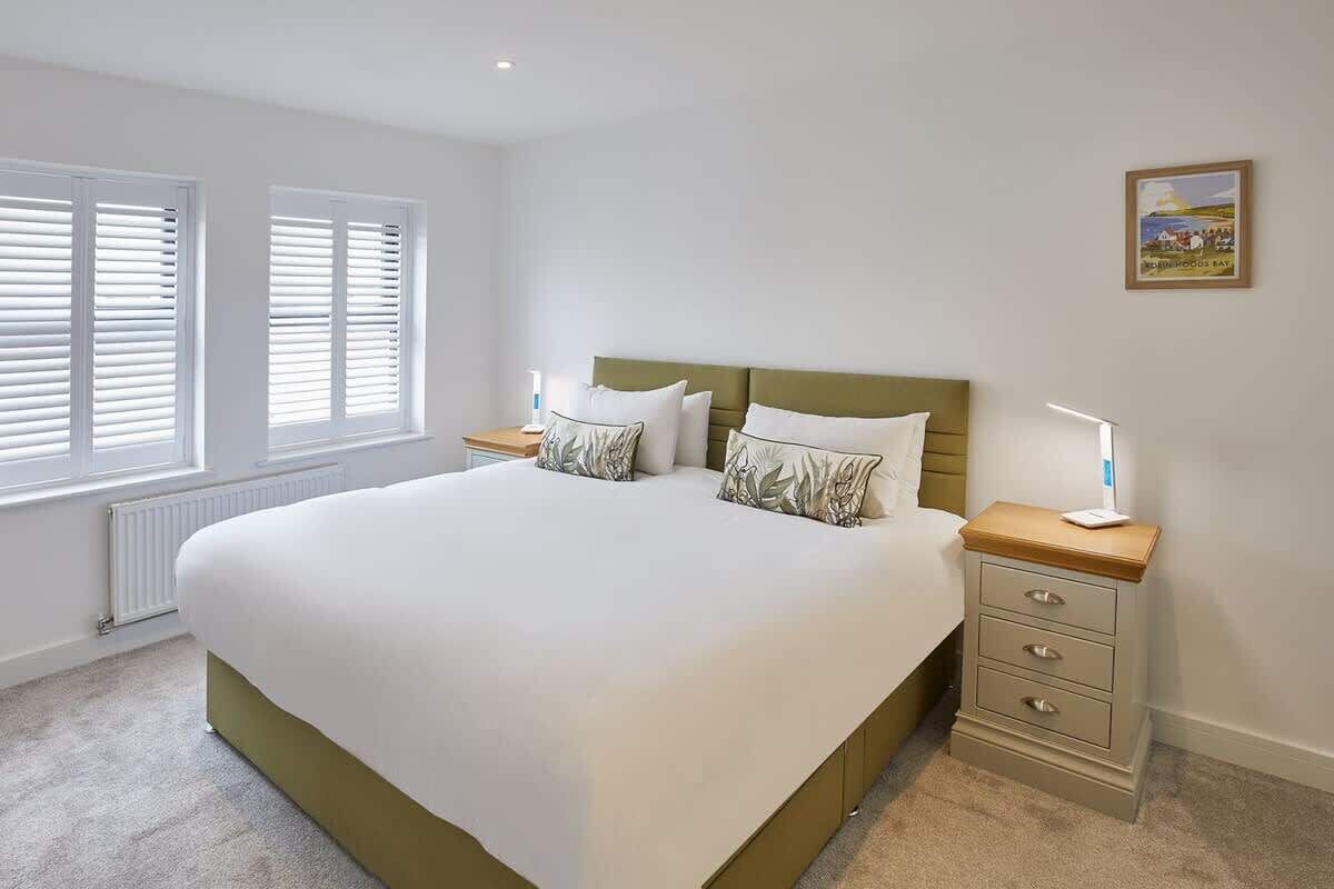 A bedroom with a large bed, two bedside tables, and a window with blinds.