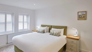 Une chambre à coucher avec un grand lit, deux tables de chevet et une fenêtre avec des stores.