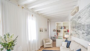 Una sala de estar con un sofá blanco, una alfombra azul, un sillón blanco y una estantería con libros y adornos.