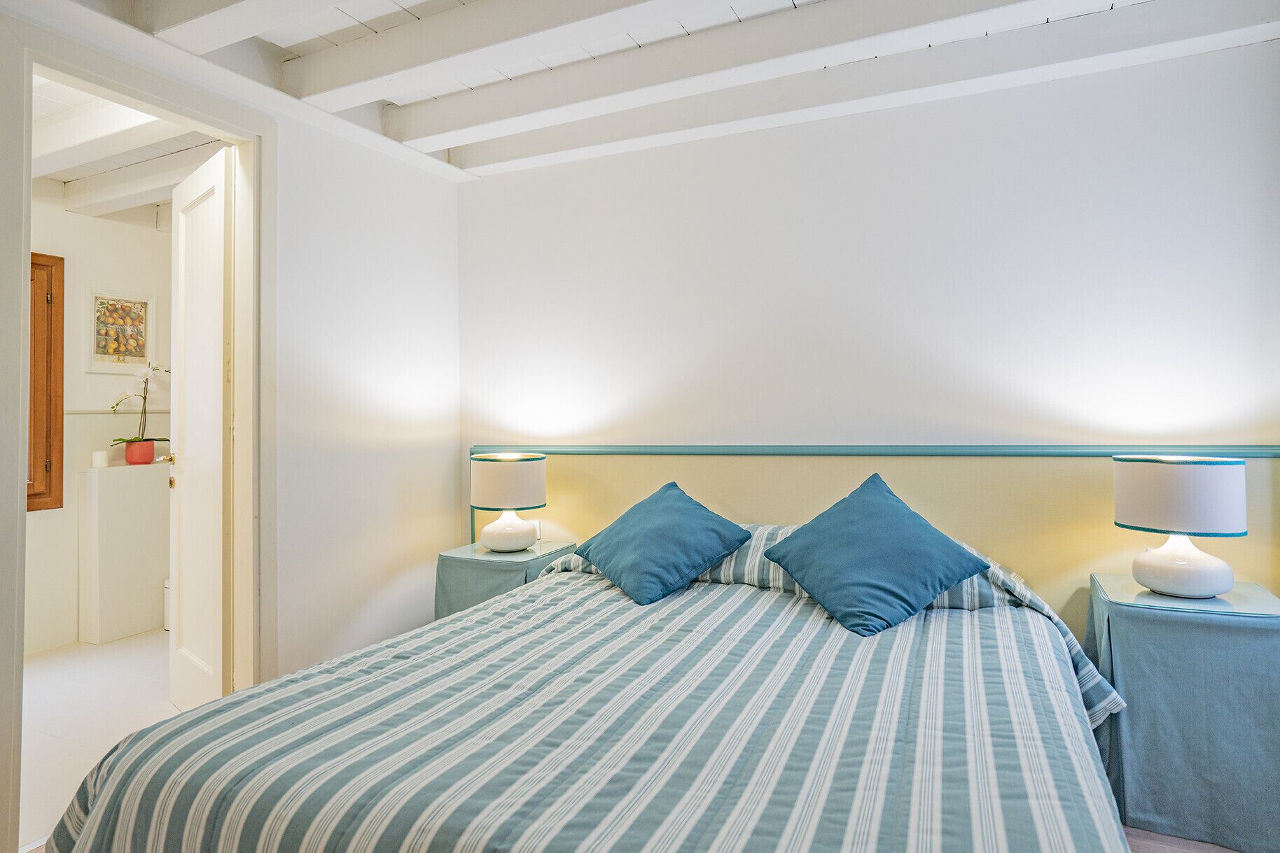 A bedroom with a bed, two bedside lamps, and a door with a picture frame.